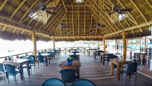Een openluchtrestaurant met rieten daken, houten tafels en stoelen.