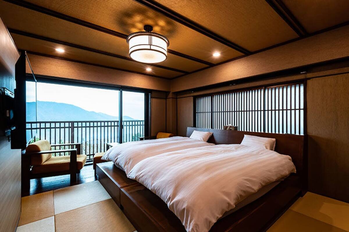 Une chambre avec un grand lit, un petit coin salon et une vue sur les montagnes par la fenêtre.
