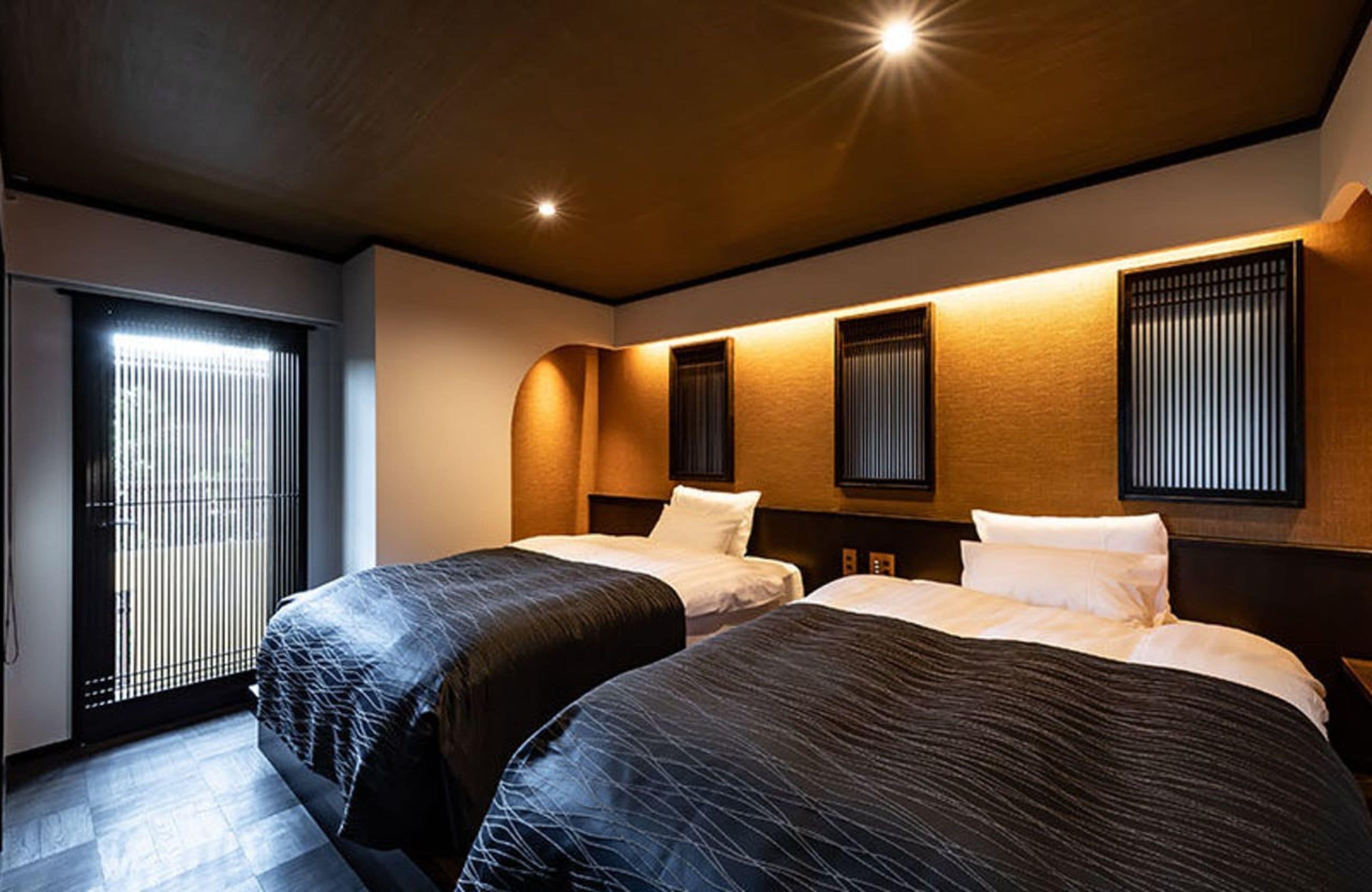 A hotel room with two beds, a large window with blinds, and a ceiling with recessed lighting.