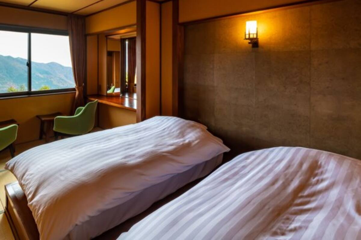 Une chambre d’hôtel avec deux lits, une grande fenêtre donnant sur les montagnes, un bureau et une chaise.
