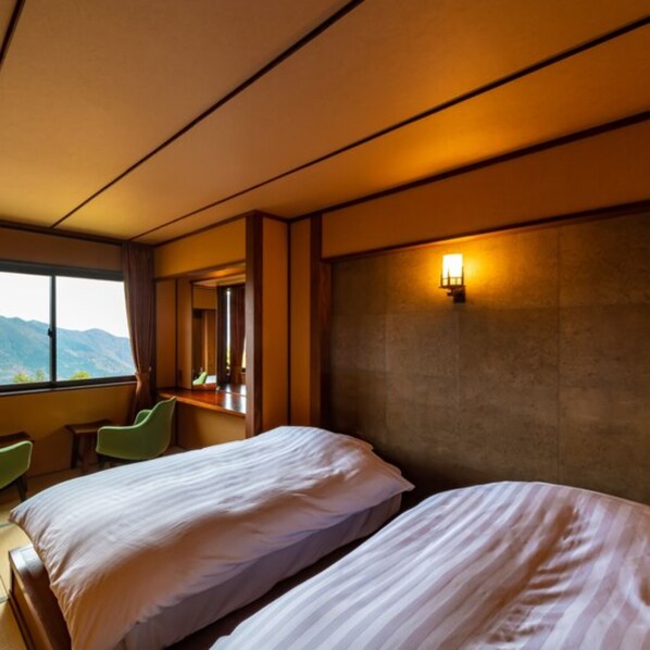 A hotel room with two beds, a large window with a mountain view, a desk, and a chair.