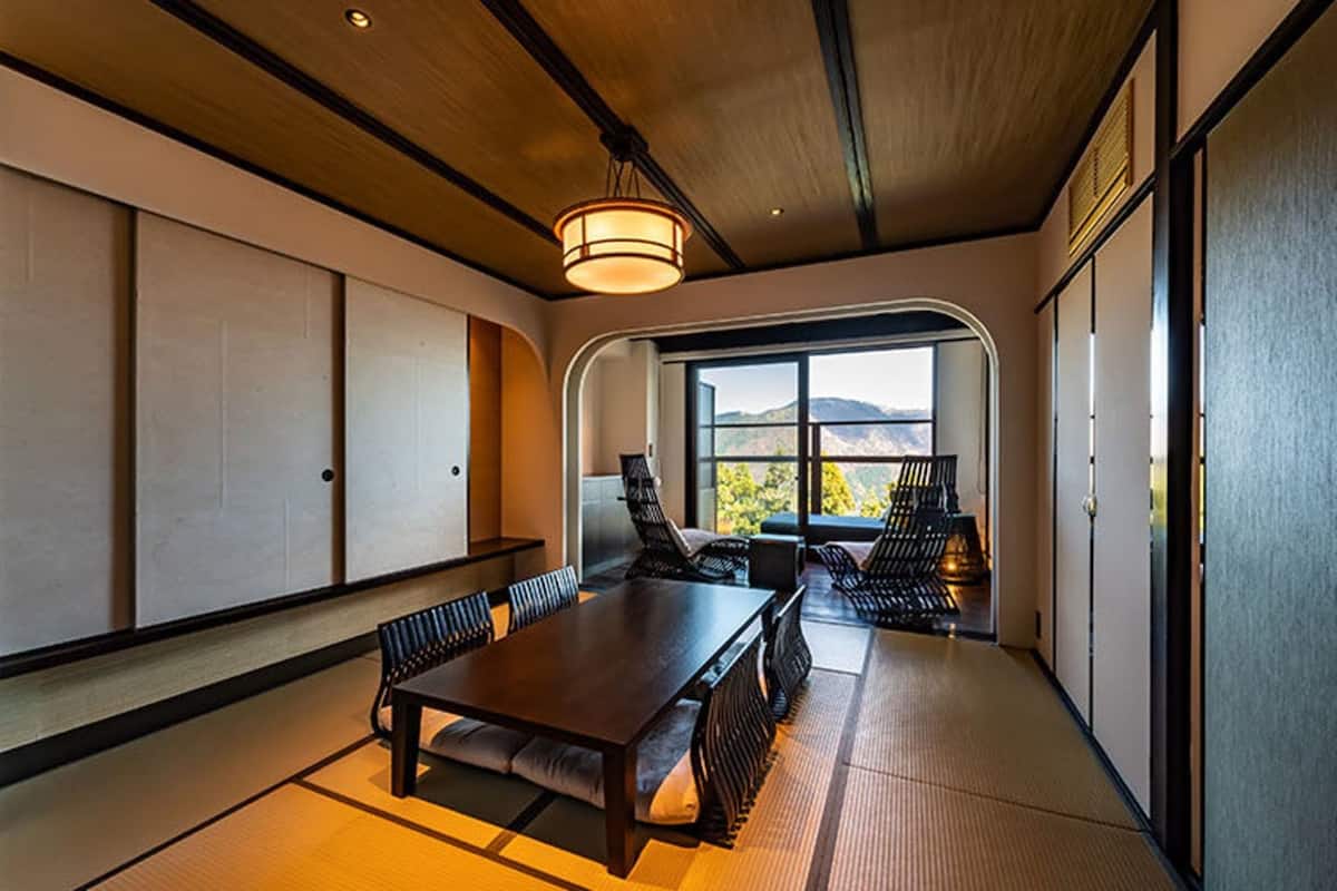 Une pièce de style japonais traditionnel, avec un sol recouvert de tatamis, une basse table en bois et des chaises rembourrées de couleur noire.