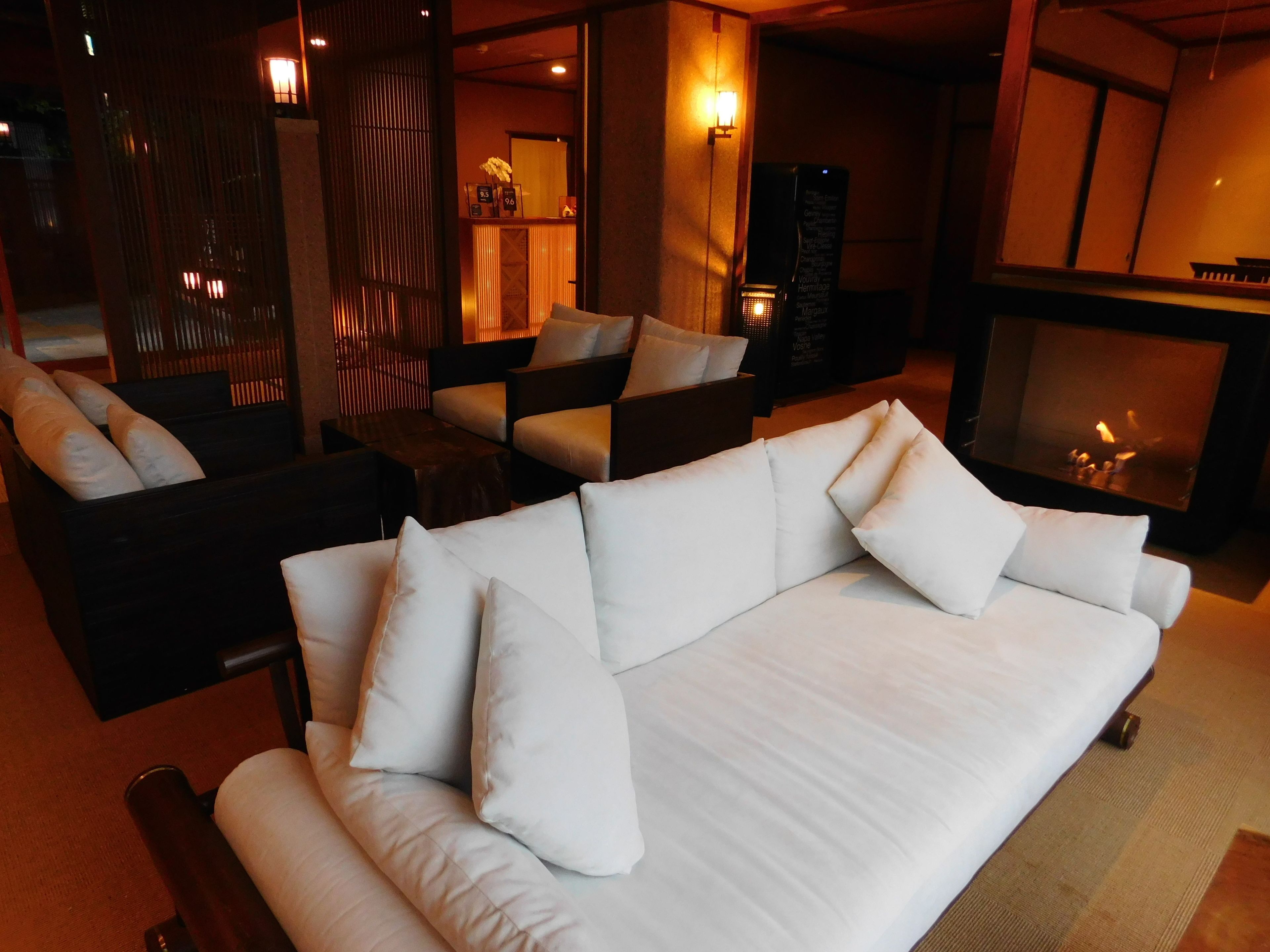 A modern living room with a white sofa, dark armchairs, a fireplace, and a wooden partition.