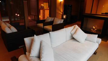 A modern living room with a white sofa, dark armchairs, a fireplace, and a wooden partition.