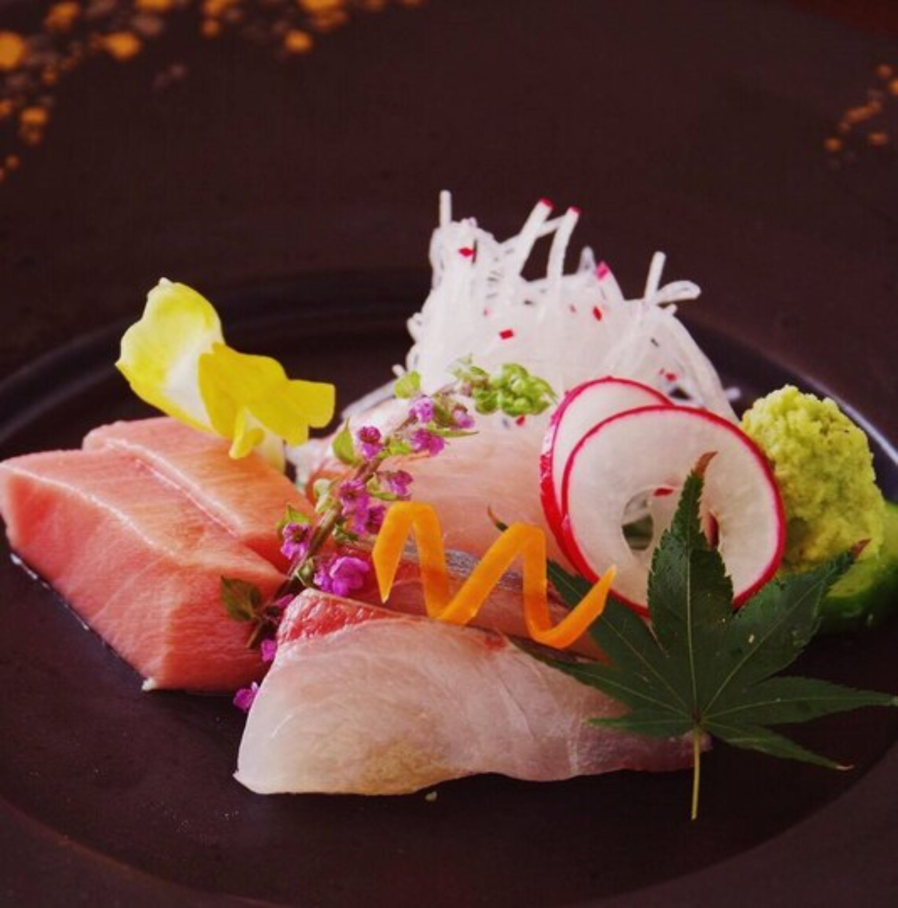 Ein Teller mit Sashimi, Rettichscheiben und einer Dekoration aus Blumen und Blättern.