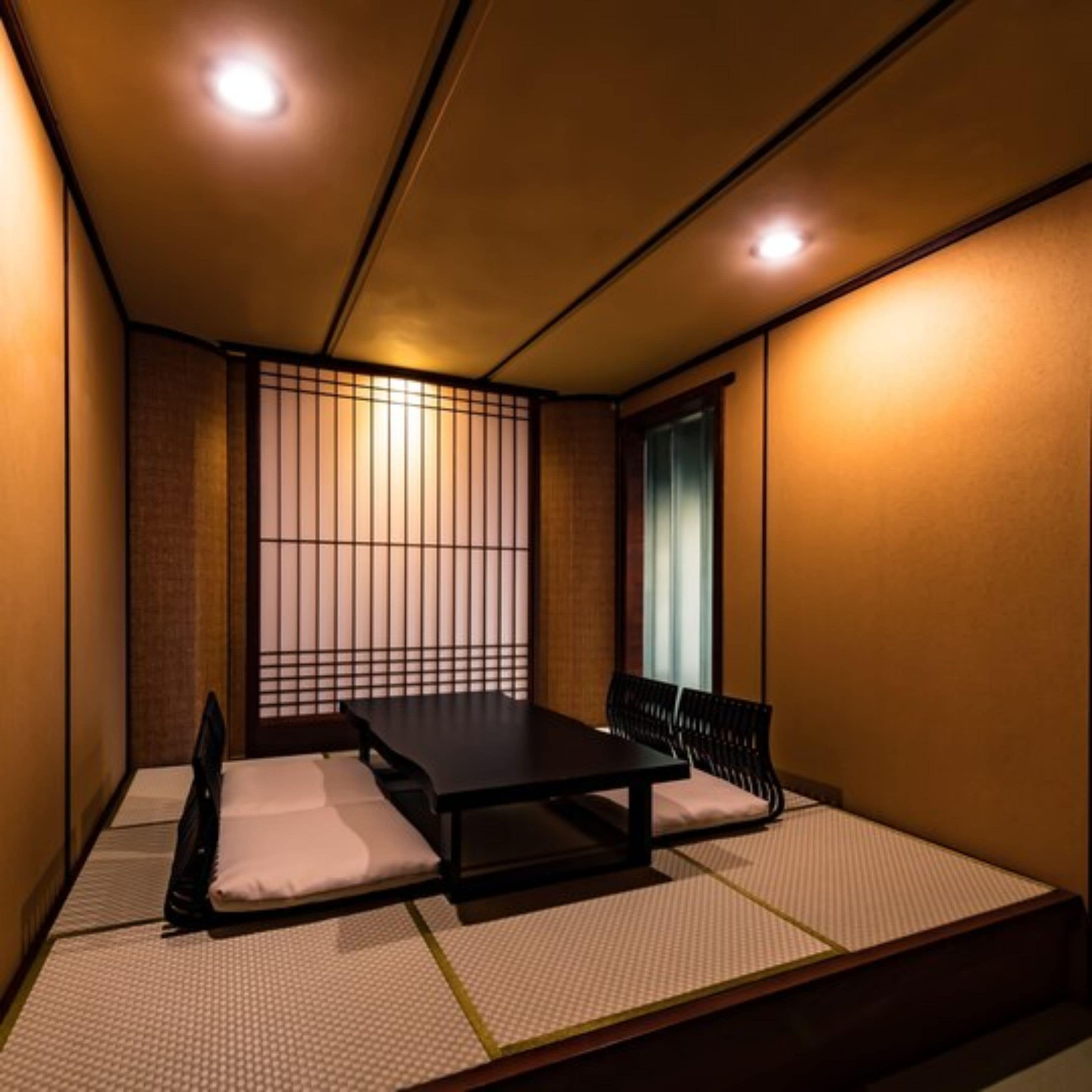 Een traditionele Japanse kamer met tatami vloerbedekking, een lage tafel en zwarte stoelen.