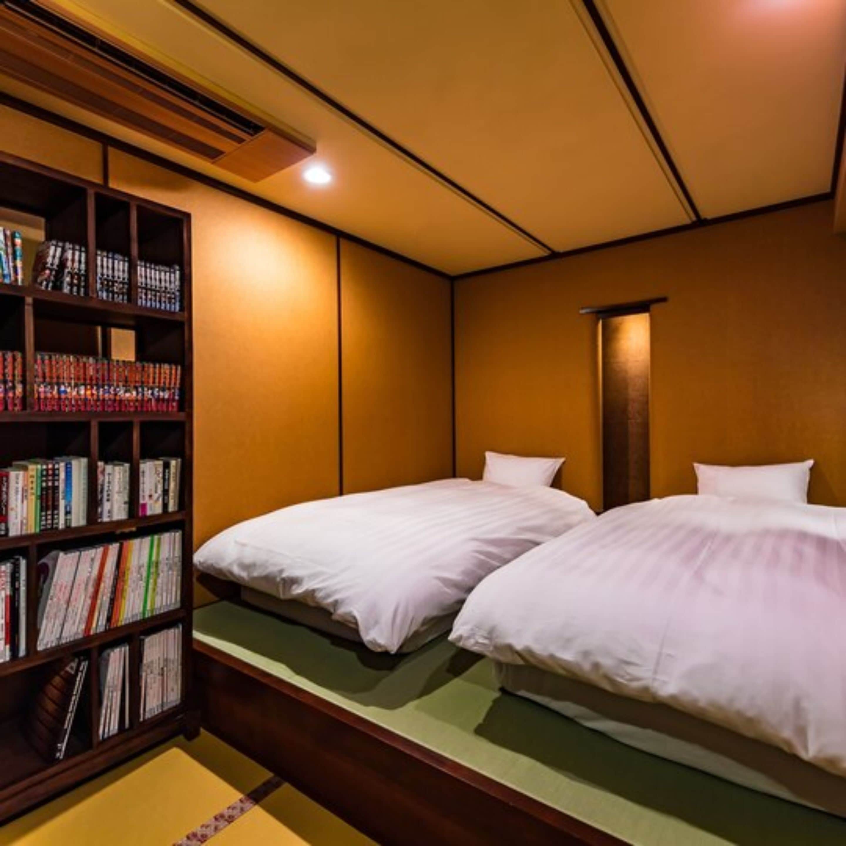 Ein Hotelzimmer mit zwei Betten, einem Bücherregal und einer traditionellen japanischen Wand.