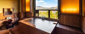 A modern bathroom with a large soaking tub, wooden paneling, a mirror, and a view of mountains through a large window.