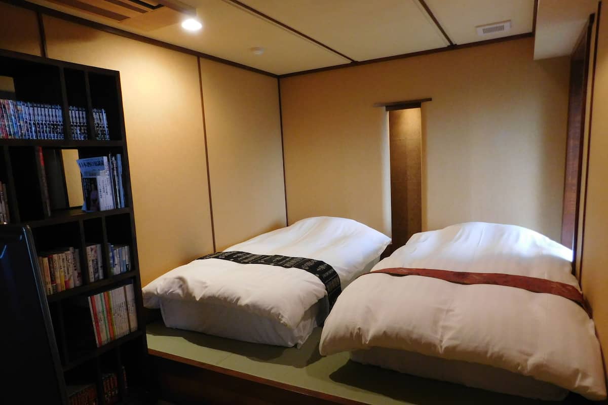 Une chambre d’hôtel avec deux lits, une bibliothèque remplie de livres et une tête de lit en bois.