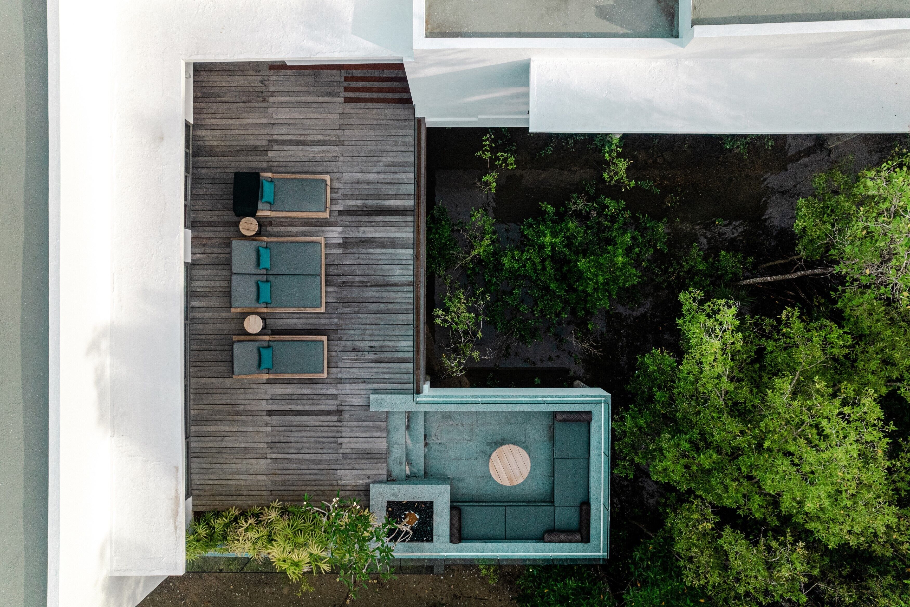 An aerial view of a modern outdoor patio with a wooden deck, a seating area with cushions, and a circular table.