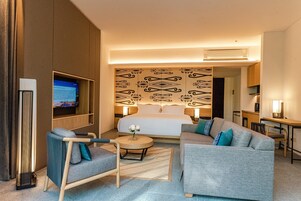 Una habitación de hotel moderna con una cama grande, un sofá, una pequeña mesa redonda y un televisor en la pared.