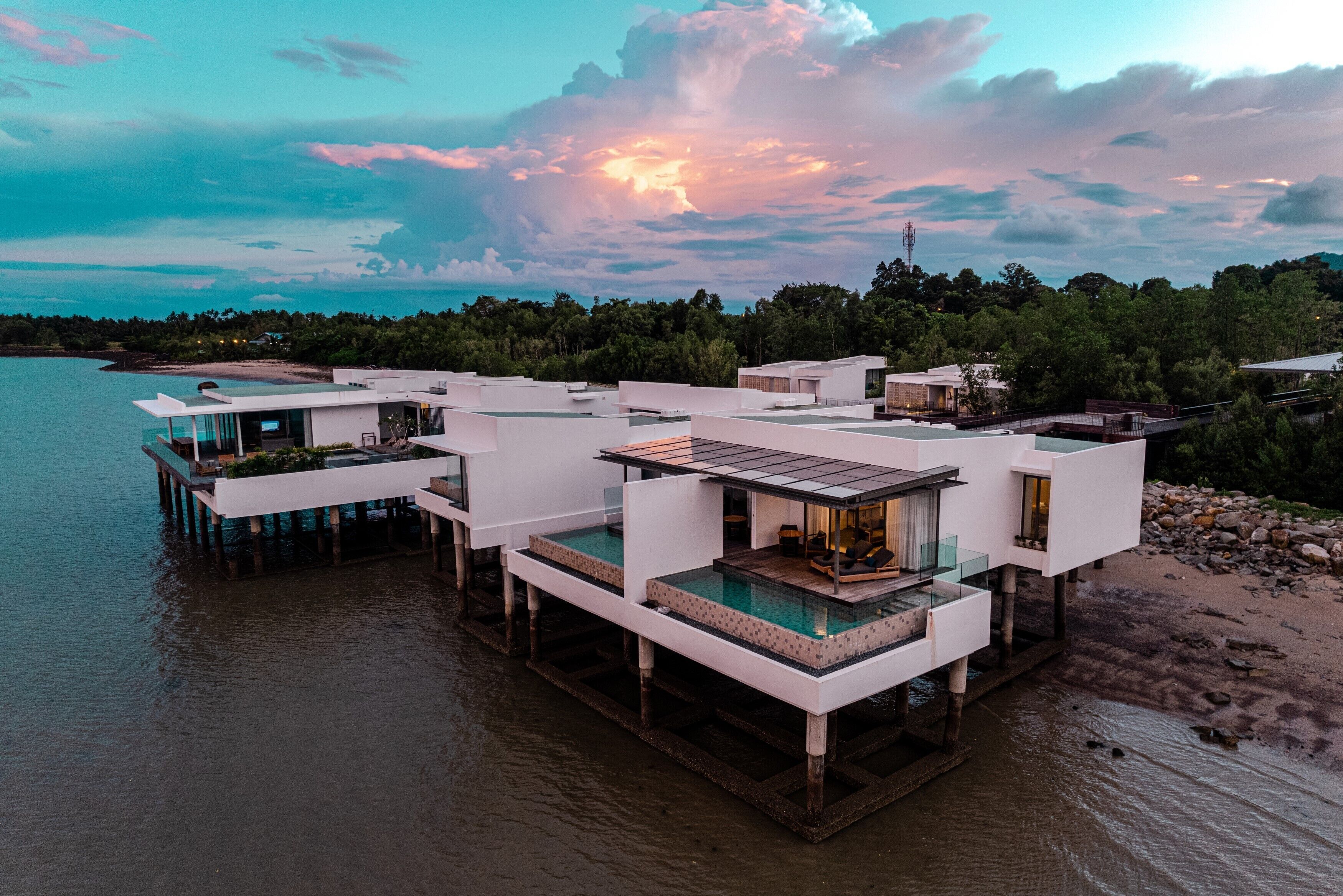 A waterfront property with multiple modern structures, including a large glass-enclosed pool area and elevated walkways.