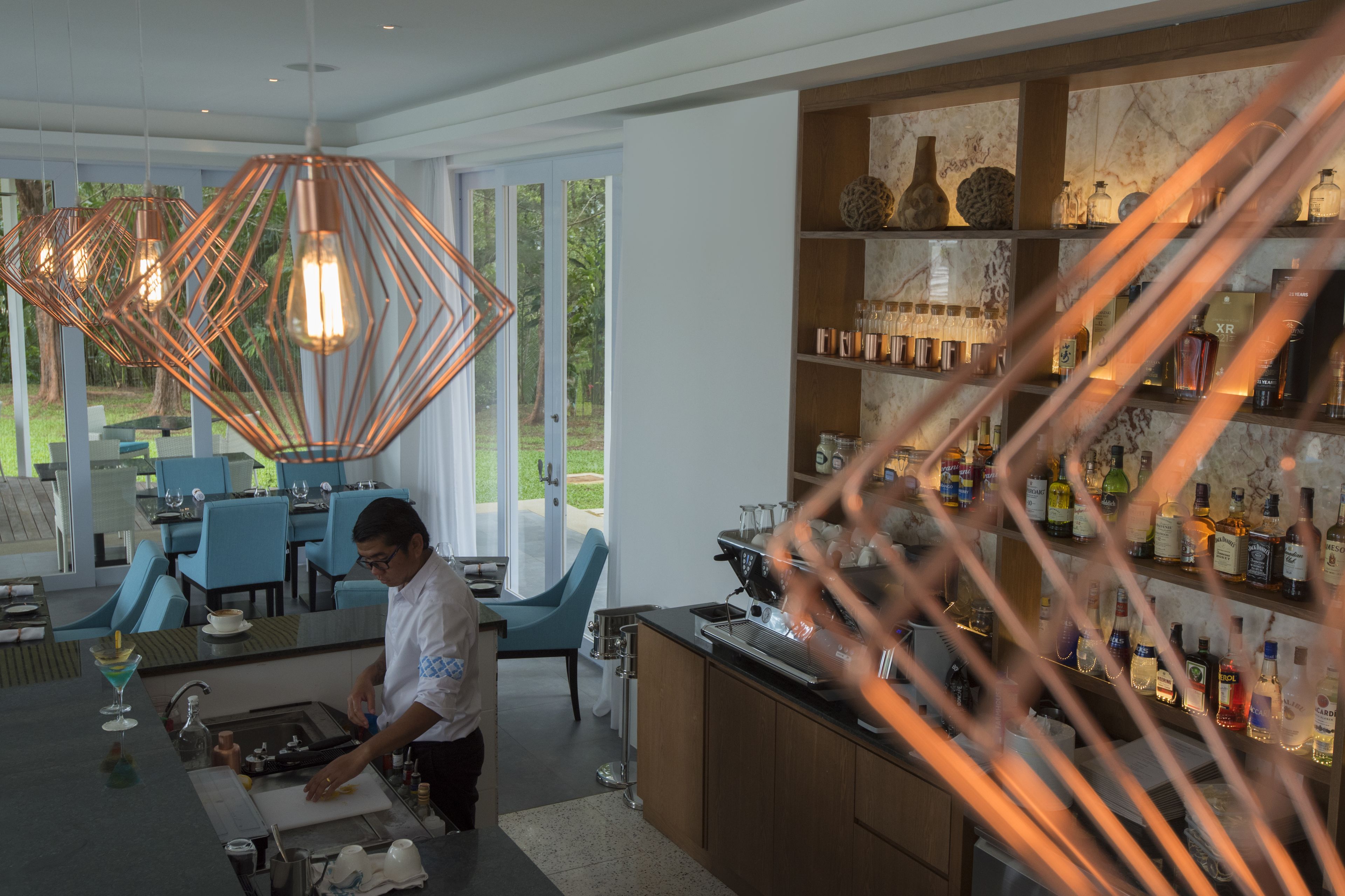 A modern kitchen with a bar area, featuring copper pendant lights, a countertop with a coffee machine, and a wine bottle display.