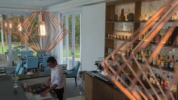 A modern kitchen with a bar area, featuring copper pendant lights, a countertop with a coffee machine, and a wine bottle display.