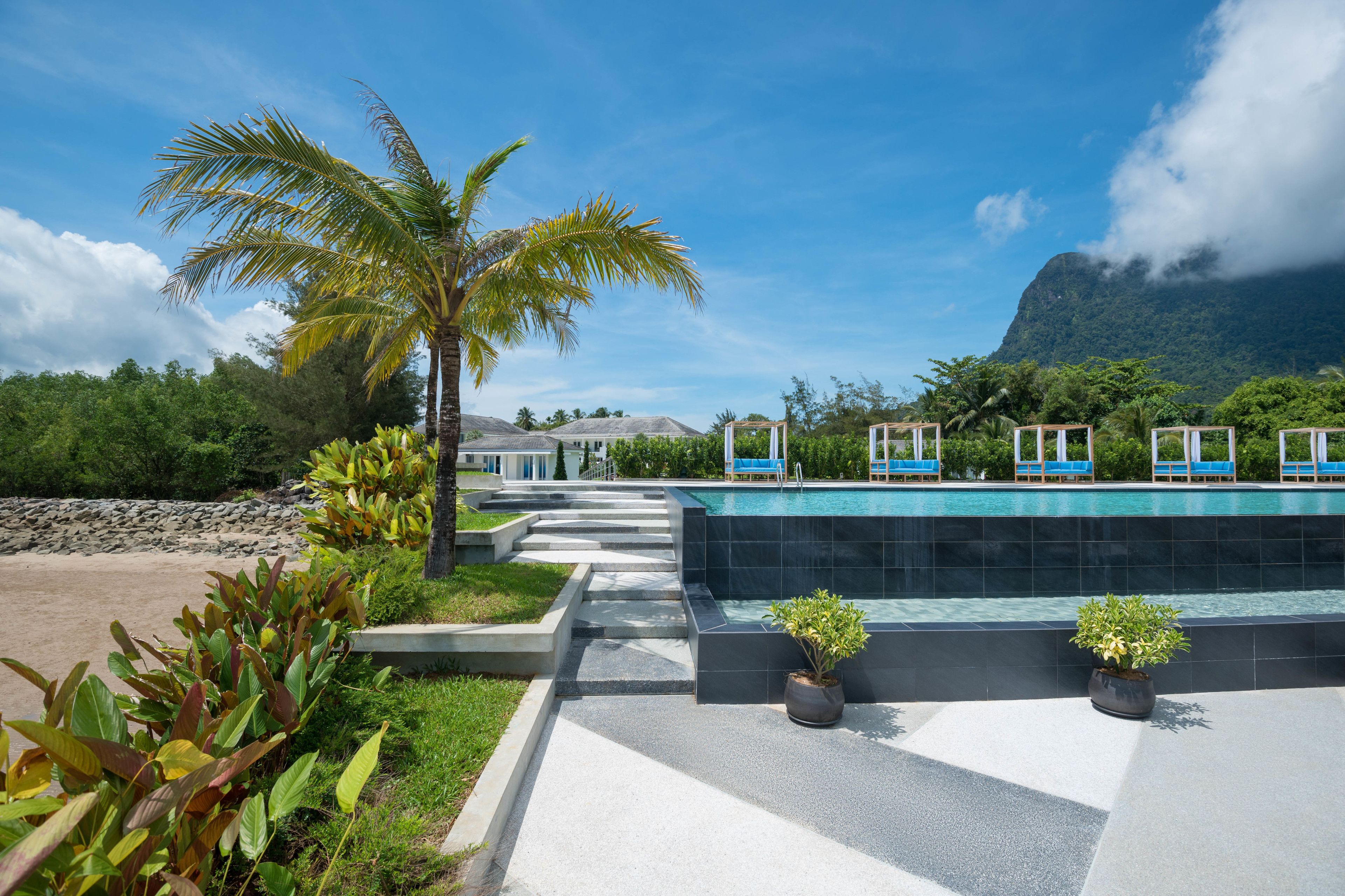 A pool area with steps leading to a pool, surrounded by greenery and a mountain in the background.