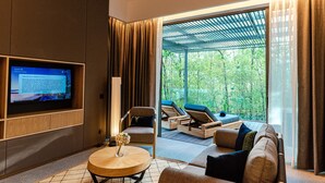 A modern living room with a flat-screen TV, a round coffee table, and a sofa. There is a sliding glass door leading to an outdoor area with lounge chairs. - Cove 55 (Kuching)