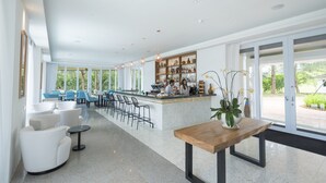 A spacious, modern bar area with a long counter, multiple seating options including bar stools and chairs, and a large window providing a view of the outdoors. - Cove 55 (Kuching)
