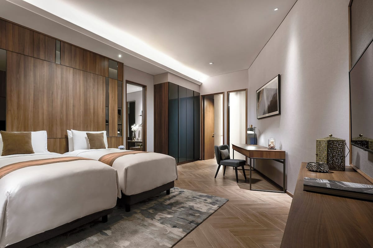 A modern hotel room with two beds, a desk, and a large mirror.