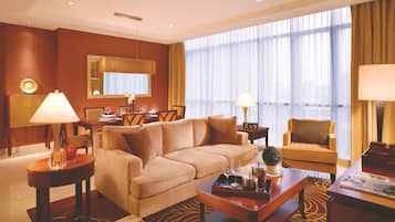 A hotel room with a sofa, armchairs, a dining table set, and a large window with curtains.