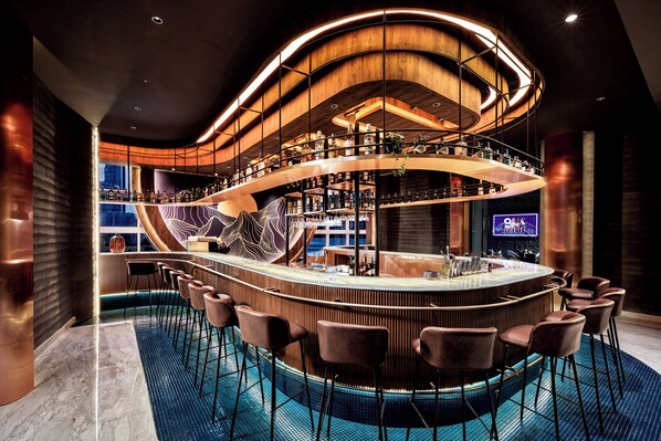 A modern bar with a curved design, multiple levels, and a pool area. - Oakwood Premier Cozmo Jakarta (Jakarta)