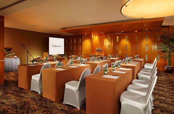 A conference room with long tables, white chairs, and floral centerpieces.