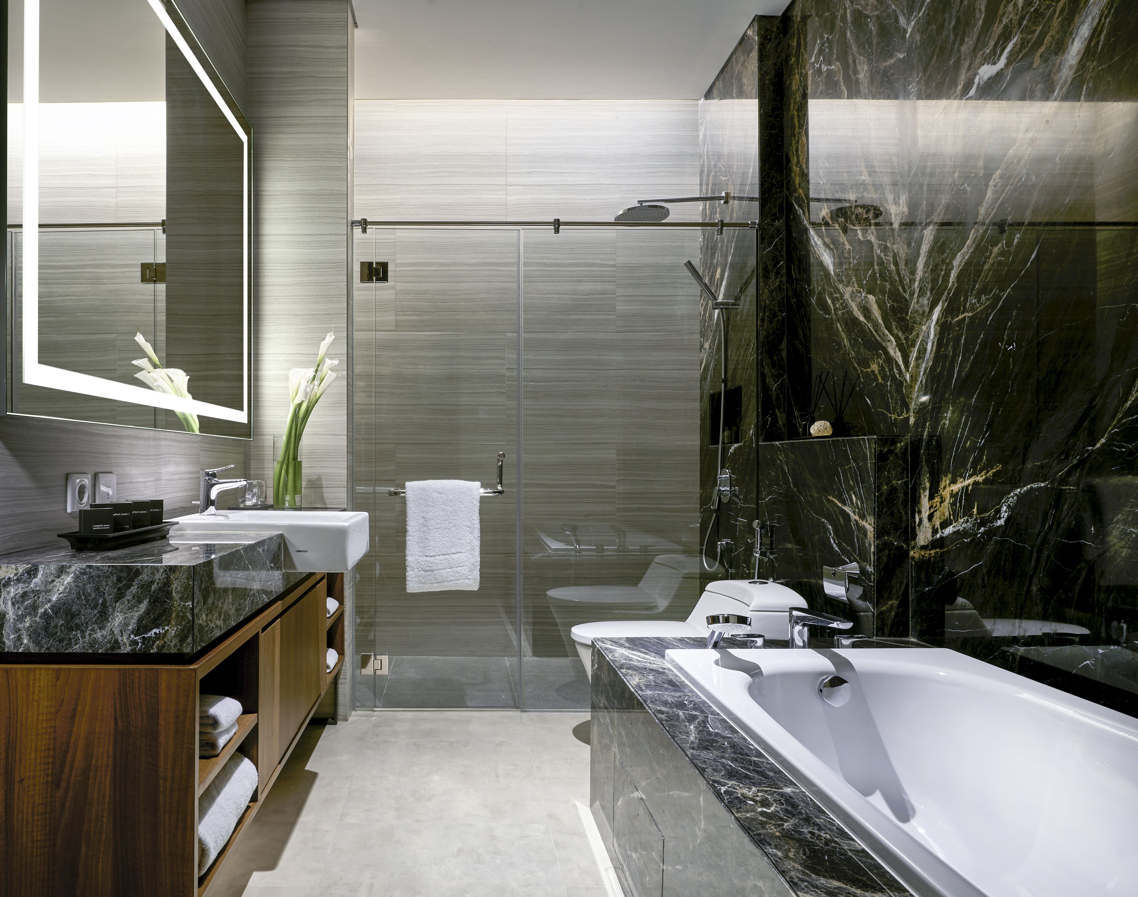 A modern bathroom with a large bathtub, a glass-enclosed shower, and a vanity with a marble countertop.