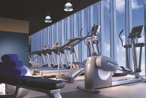 A gym with treadmills, ellipticals, and a bench. - Oakwood Premier Cozmo Jakarta (Jakarta)