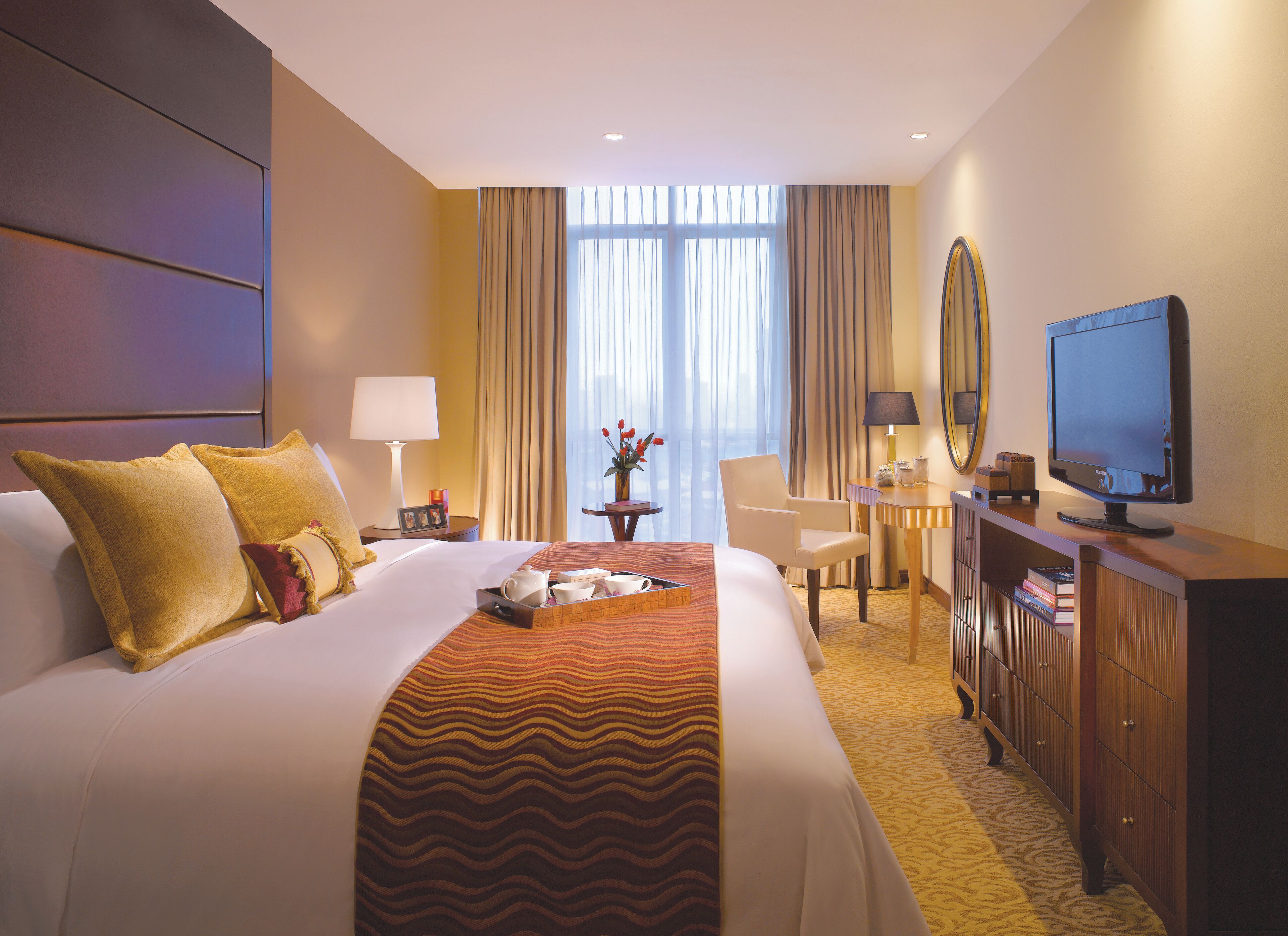 A hotel room with a large bed, a desk with a computer, a television, and a small table with a vase of flowers.