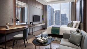 A modern hotel room with a large bed, a desk with a flat-screen TV, a comfortable sofa, and a view of the city skyline. - Oakwood Premier Cozmo Jakarta (Jakarta)