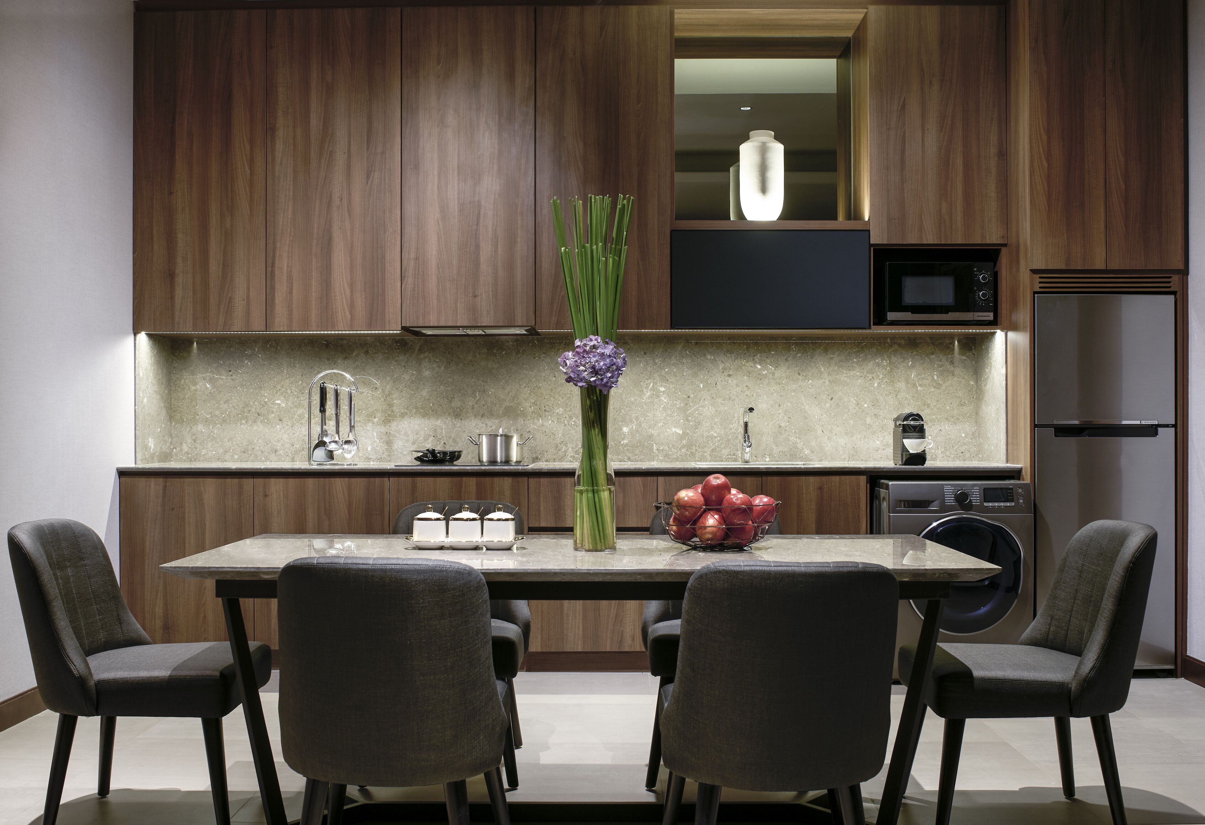 Una cocina moderna con armarios de madera, una isla central con sillas, un lavamanos, un microondas y un refrigerador.