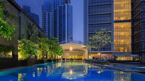 A swimming pool surrounded by tall buildings, with a covered area and lounge chairs. - Oakwood Premier Cozmo Jakarta (Jakarta)