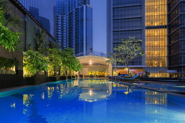 A swimming pool surrounded by tall buildings, with a covered area and lounge chairs. - Oakwood Premier Cozmo Jakarta (Jakarta)