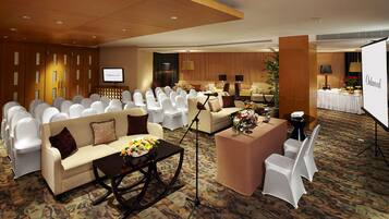 A conference room with rows of white chairs, a sofa, a coffee table with flowers, and a projection screen.
