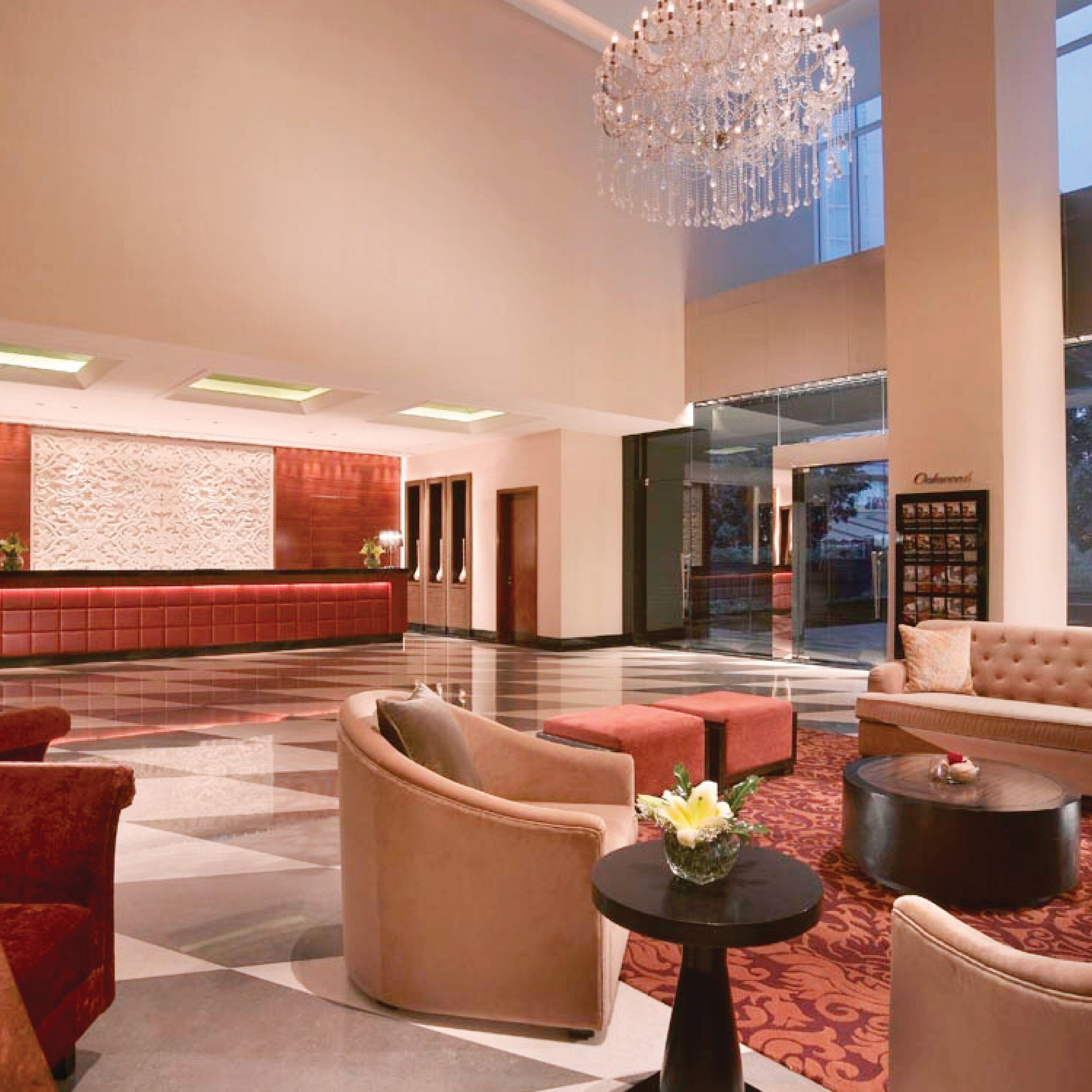 A spacious lobby with a red seating area, a large chandelier, and a view of the city through large windows.