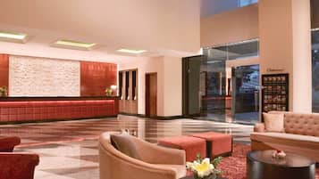 A spacious lobby with a red seating area, a large chandelier, and a view of the city through large windows.