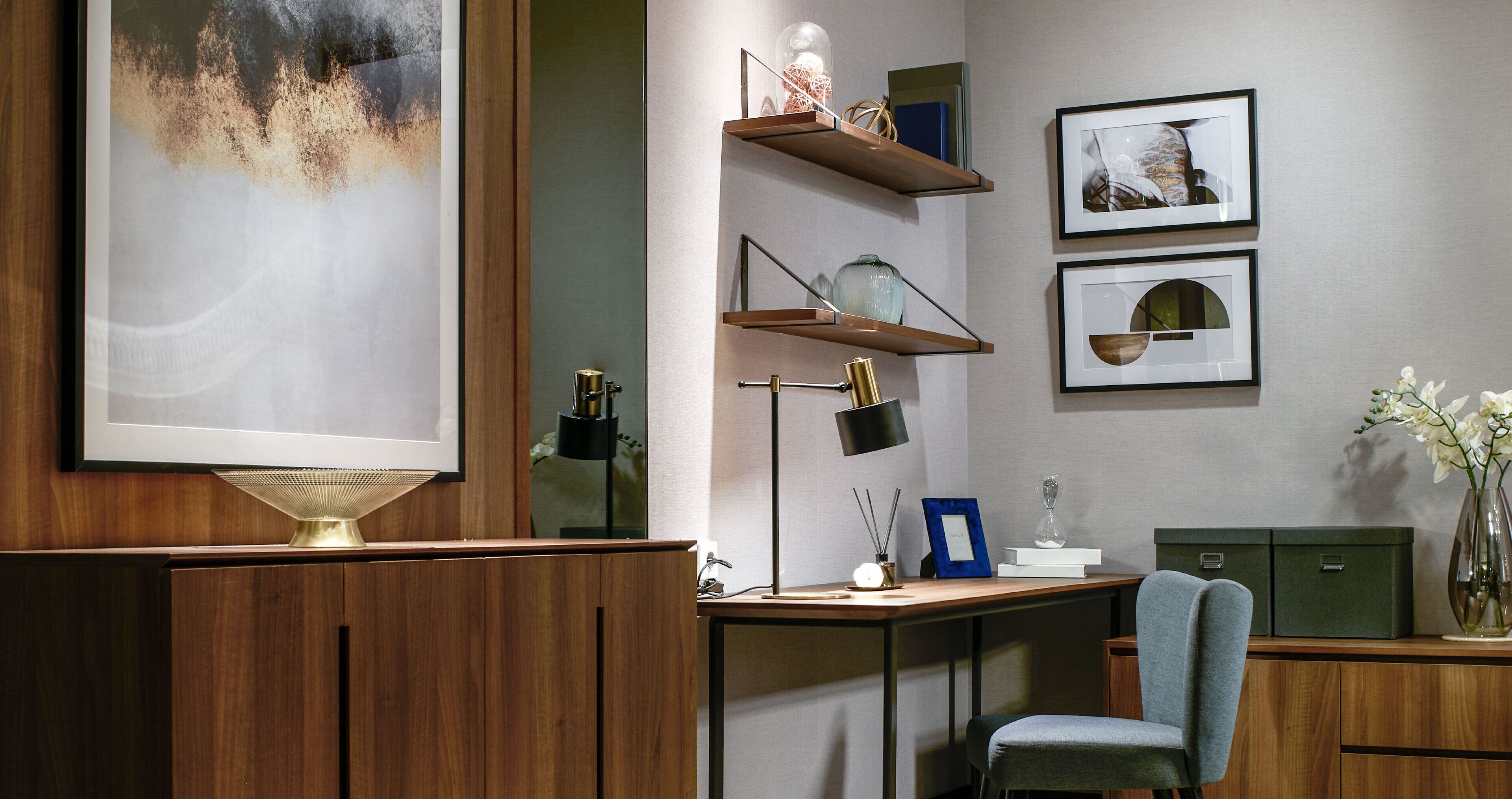 Un espace de bureau moderne avec un bureau en bois, une chaise bleue, un grand tableau abstrait, des étagères ornées d’objets décoratifs et des tableaux encadrés accrochés au mur.