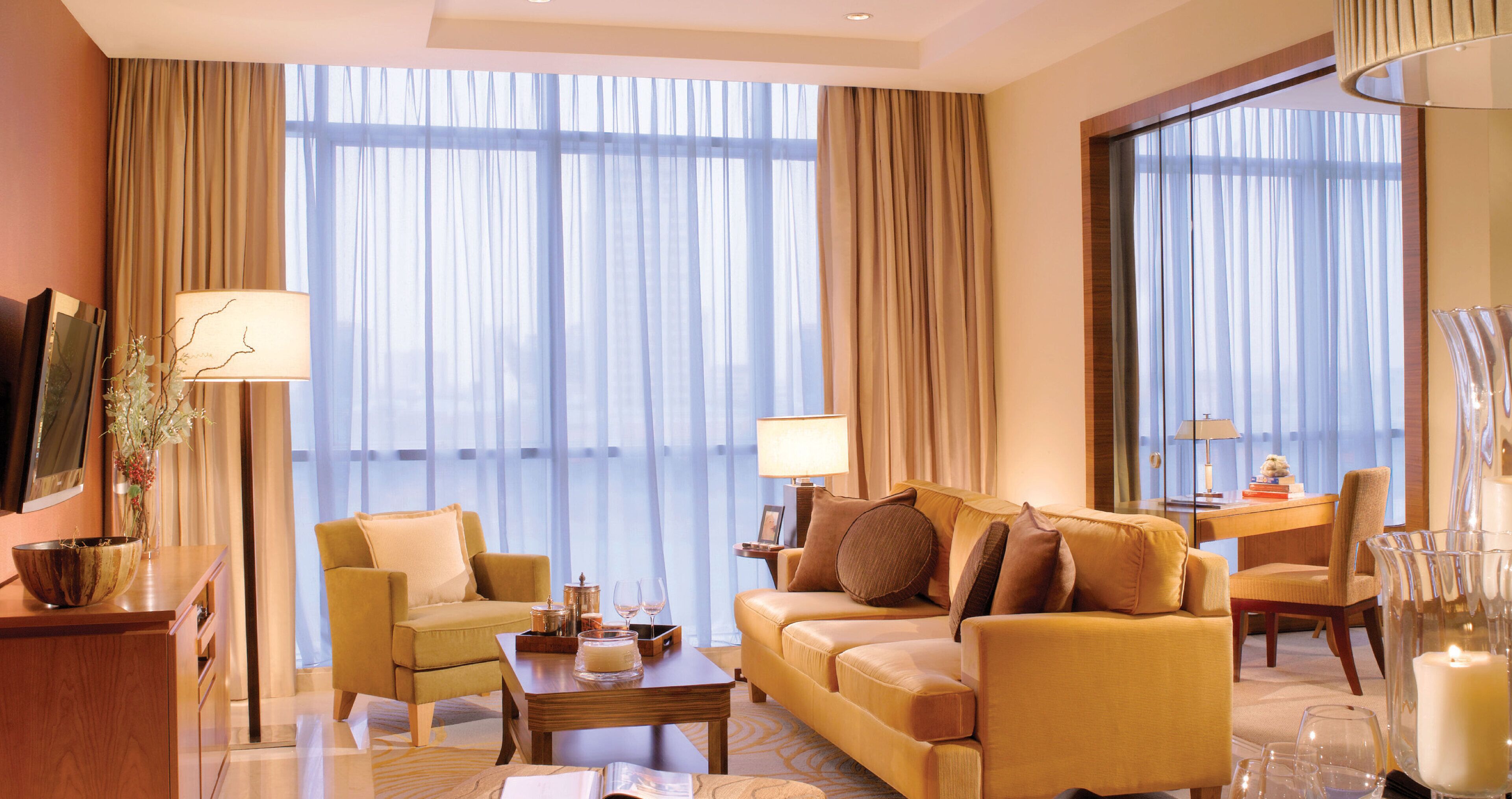 A hotel room with a sofa, armchairs, a coffee table, and a desk with a lamp.