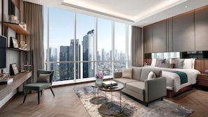 A modern hotel room with a large window, a sofa, a bed, a TV, and a small table with a vase of flowers. - Oakwood Premier Cozmo Jakarta (Jakarta)