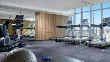 A modern gym with multiple treadmills, a weight bench, and a pair of dumbbells.
