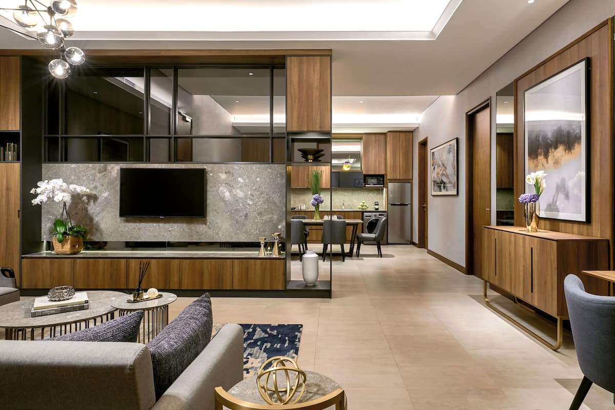 A modern living room with a sofa, coffee table, and a TV mounted on a stone wall. There is a dining area with a table and chairs in the background.