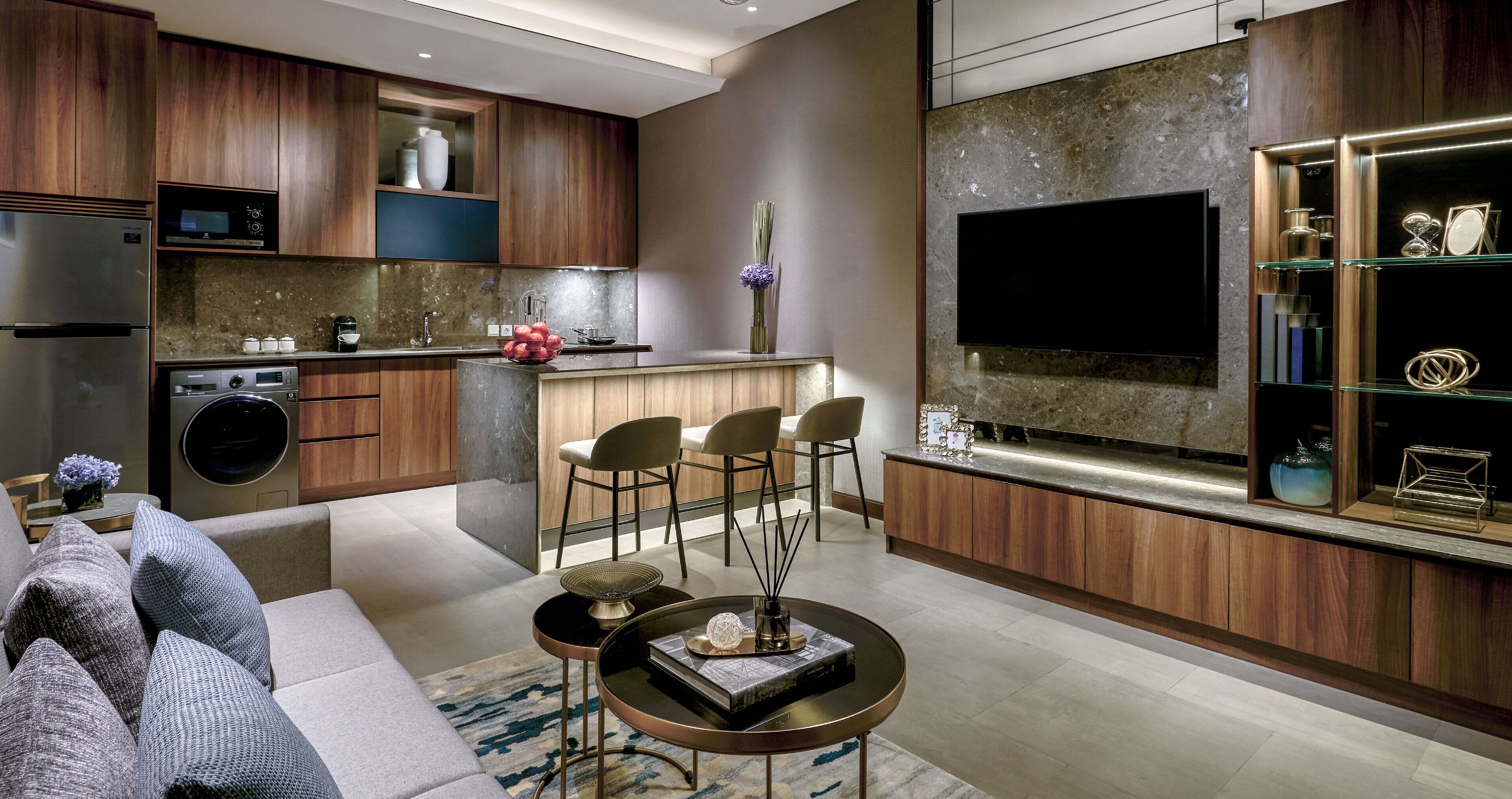 A modern kitchen with wooden cabinets, a built-in oven, and a large flat-screen TV above the counter.