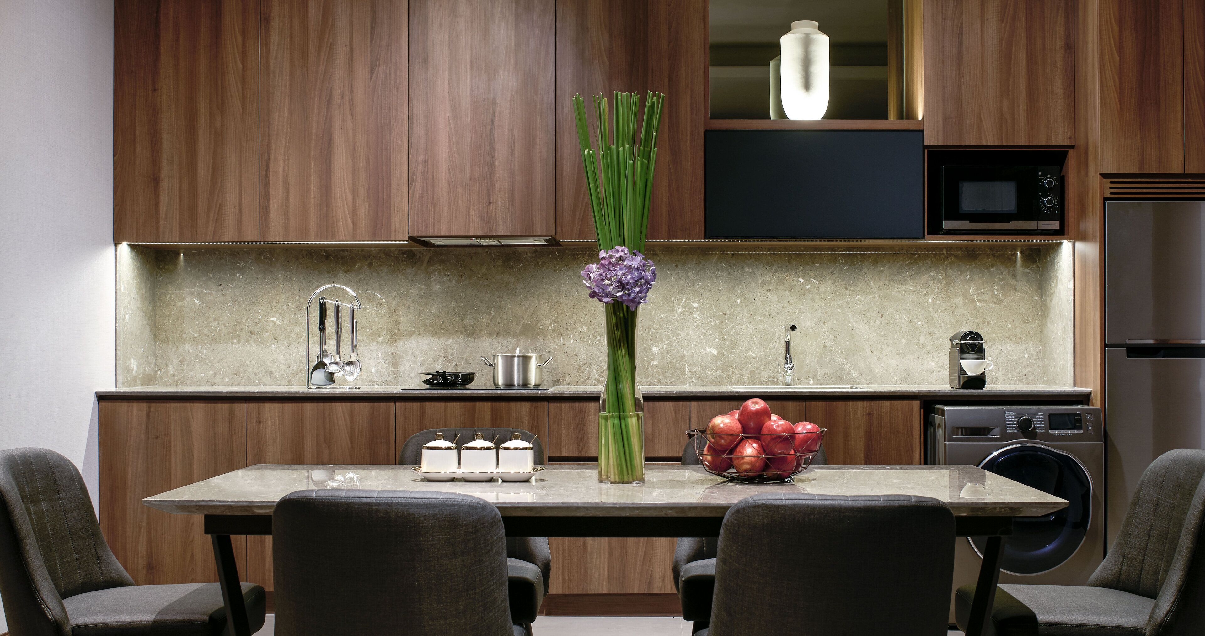 A modern kitchen with wooden cabinets, a granite countertop, a built-in microwave, and a stainless steel refrigerator.