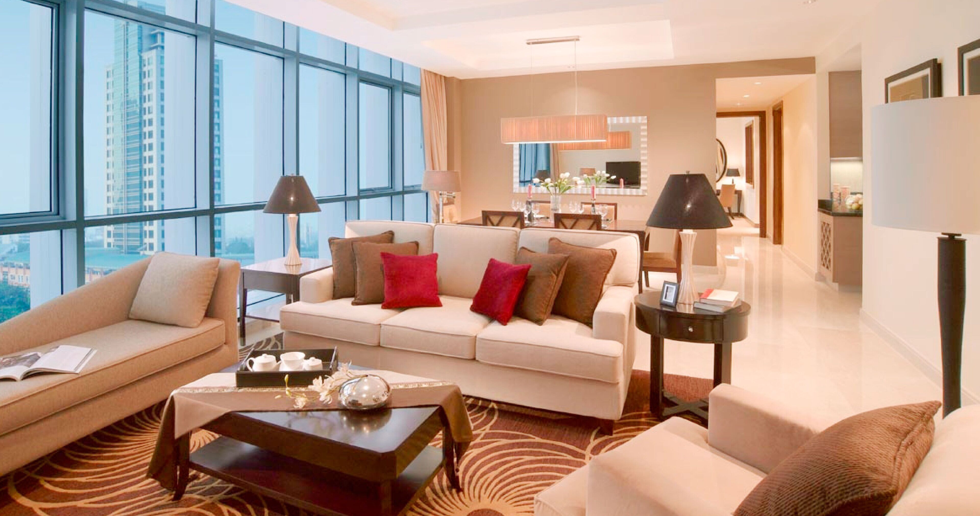 A modern hotel room with a large window, a sofa, a coffee table, and a dining area.
