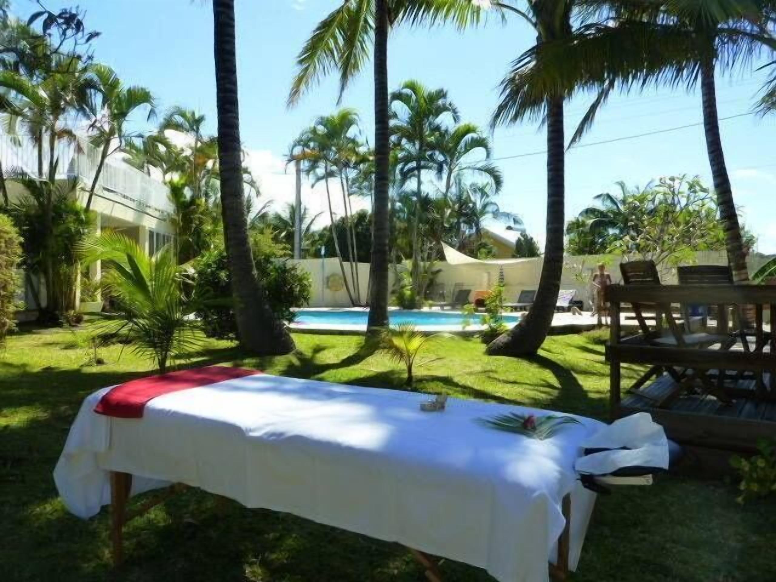 A poolside area with a covered table, lounge chairs, and palm trees.