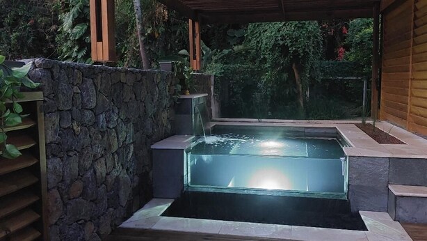 Jacuzzi en una zona exterior coberta amb parets de pedra i paviment de fusta.