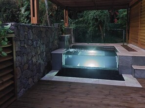 Un bain à remous situé dans un espace extérieur abrité, avec des murs en pierre et un plancher en bois.