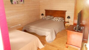 Dormitori d'una cabana de fusta amb dos llits, un reposacapses de fusta, una televisió i un quadre floral a la paret.
