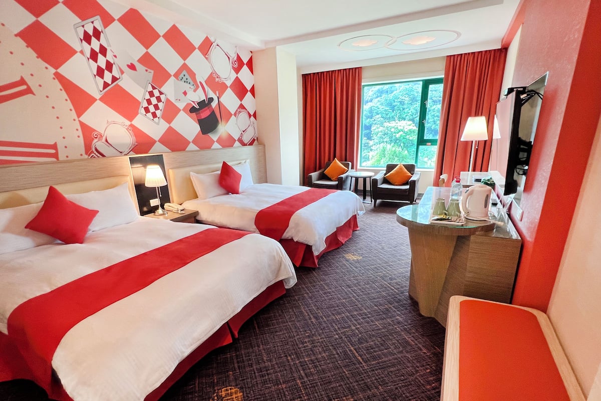 A hotel room with two beds, a desk, a chair, a TV, and a window with curtains.