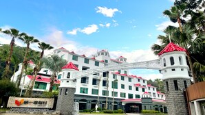 A multi-story hotel with a white facade and red roofs, featuring a central archway and surrounded by palm trees. - Uni-Resort Mawutu (Guanxi)