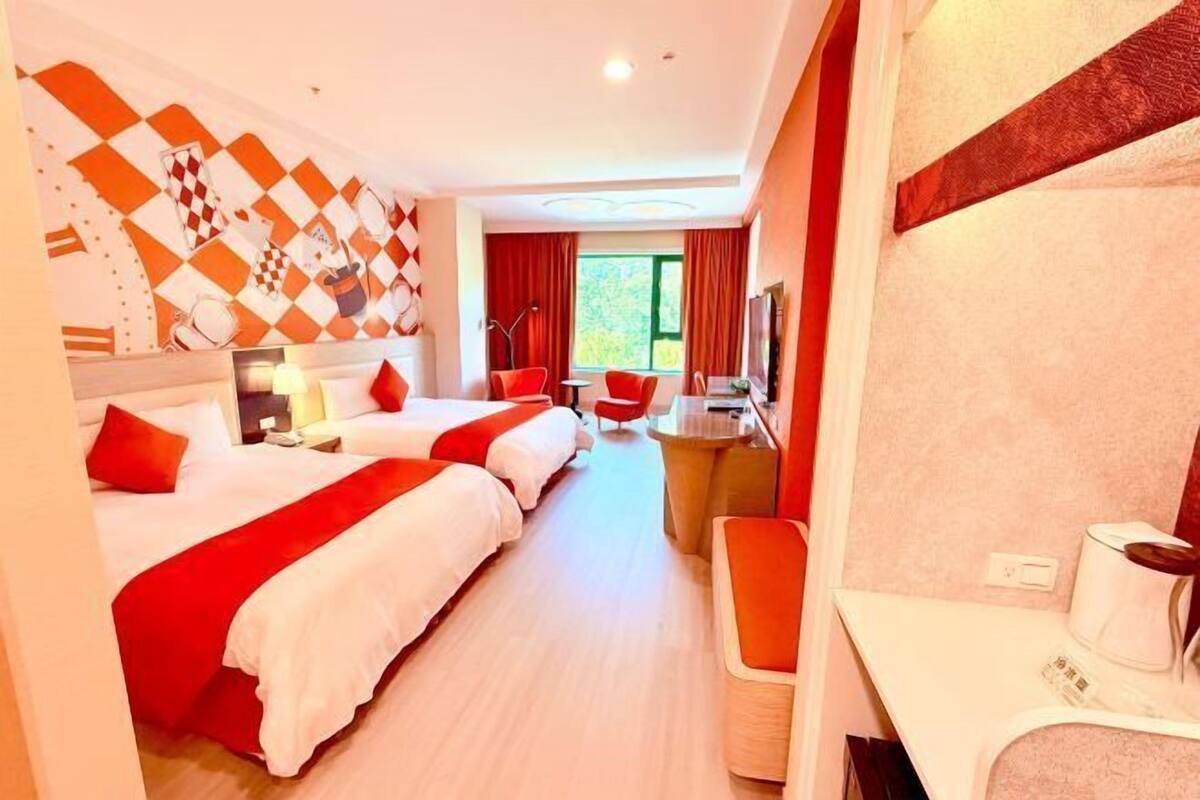 A hotel room with two beds, a desk, a chair, and a TV.